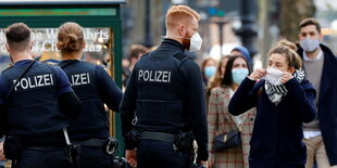 Mehrere Polizisten ermahnen eine Frau, ihre Maske zu tragen