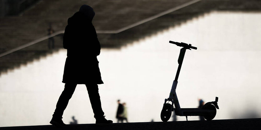 Eine Frau läuft auf einen E-Roller zu, Gegenlichtaufnahme