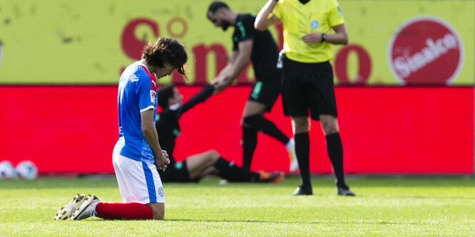 Fußballer Jae-Sung Lee von Holstein Kiel kniet mit gesenktem Kopf auf dem Rasen.