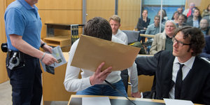 Der Angeklagte verdeckt sein Gesicht mit einem großen Briefumschlag