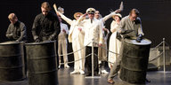 Mann in weißer Uniform steht zwischen Trommlern auf der Bühne
