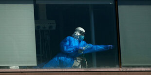 Ein Mann in Schutzkleidung steht an einem Fenster eines Krankenhauses