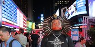 Ein mann mit Federschmuck steht auf dem beleuchteten Times Square