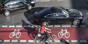 Ein Radfahrer fährt auf einem roten Radstreifen, neben ihm fährt ein Auto