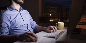 Ein Mann sitzt an seinem Computer in einem dunklen Zi