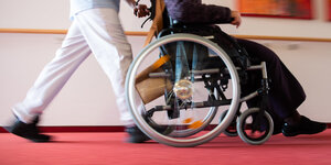 Ein Pfleger eines Pflegeheims schiebt eine Bewohnerin mit einem Rollstuhl