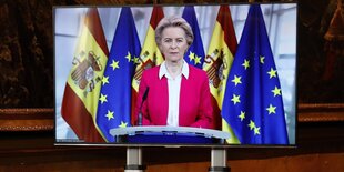 Kommissionspräsidentin Ursula von der Leyen ist auf einem Monitor zu sehen. Hinter ihr hängen euopäische und spanische Flaggen.