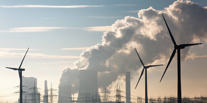 Kohlekraftwerk mit rauchenden Schloten und Windpark im Vordergrund