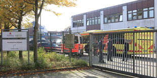 Vor einem Zaun steht ein Schild, auf dem "Ankunftszentrum" steht. Hinter dem Zaun ist ein Bus und ein Rettungswagen der Feuerwehr zu erkennen