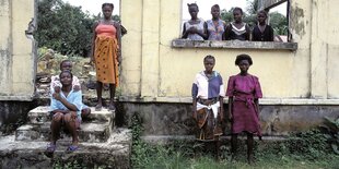 Eine Gruppe von jungen Frauen steht vor einem zerstorten Haus