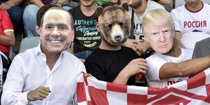 Drei Fussballfans tragen Masken: Eine Berlusconi, eine Trump- und eine Bärenmaske