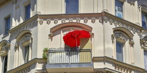 Ein Altbau-Haus mit einem Balkon auf dem sich ein roter Sonnenschirm befindet.