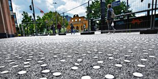 Ein betonierter Platz mit Absperrgittern hinter welchem Menschen laufen aus der Froschperspektive