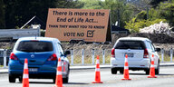 Hinter einer Autostraße steht ein Plakat mit der Aufschrift "Es gibt mehr im Sterbehilfegesetz als sie euch wissen lassen wollen"