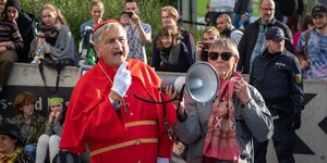 Peter Grottian in roter Kardinalsrobe spricht in ein megafon