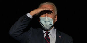 Joe Biden trägt eine Mundschutzmaske und hält sich eine Hand vor die Augen