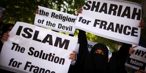 Verhüllte Frauen halten Transparente hoch, auf denen der Islam und das Schariagericht als Lösung für Farnkreich präsentiert und gefordert wird