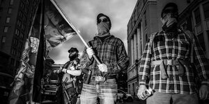 Vermummte und bewaffnete Männer halten eine Flagge. Sie gehören zu einer rechtsextremen Bewegung und unterstützten Donald Trump.