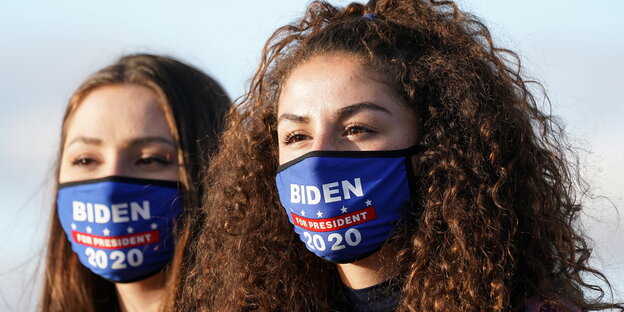 Zwei Frauen trgaen Mundschutzmasken, auf die der Name Bidens aufgedruckt ist