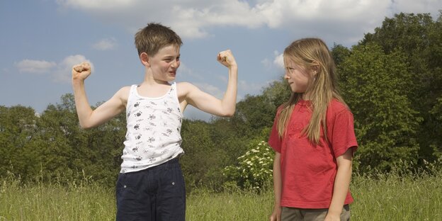 Ein kleiner Junge zeigt einem Mädchen seine Muskeln