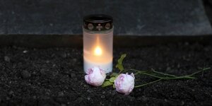 Brennendes Grablicht und rosa Blumen auf einem Friedhof