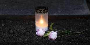 Brennendes Grablicht und rosa Blumen auf einem Friedhof