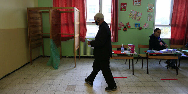 Ein Mann geht auf eine Wahlkabine zu, die in einem Klassenraum aufgebaut ist