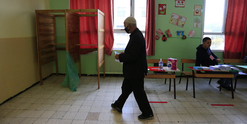 Ein Mann geht auf eine Wahlkabine zu, die in einem Klassenraum aufgebaut ist