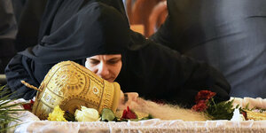 Eine Nonne küsst den Kopf des serbisch-orthodoxen Kirchenoberhaupts Amfilohije, der aufgebahrt mit goldener Kopfbedeckung in einem Sagrg liegt
