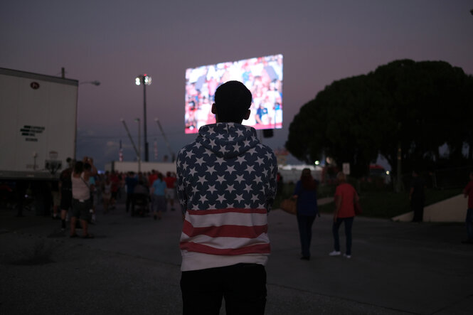 ein Mann steht eingehüllt in einer US-Flagge vor einem Bildschirm