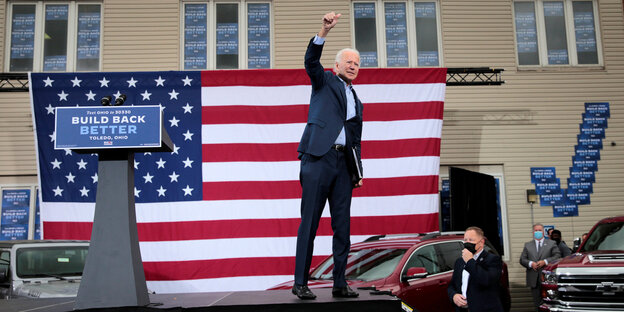 Joe biden steht auf einem Podium vor US-Flagge und reckt die Faust