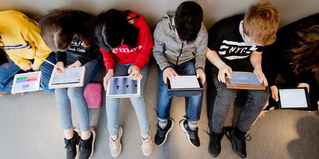 Kinder sitzen nebeneinander mit Tablet-Computern auf den Knien