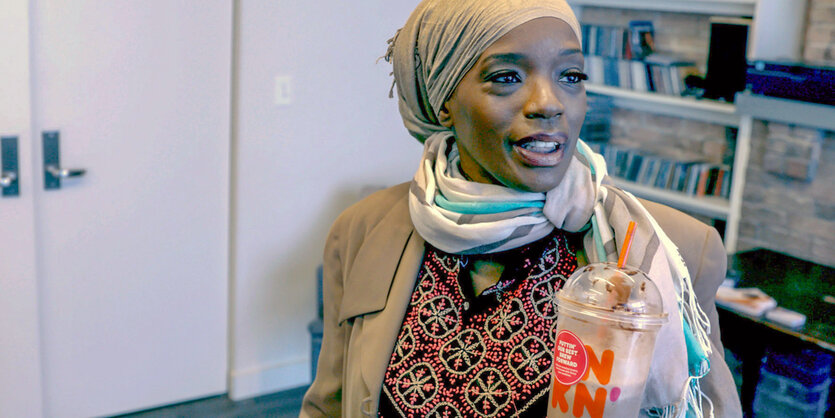 Ameena Matthews trägt ein Kopftuch und hält einen Coffe-Shake in der Hand