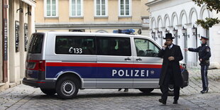 Ein Rabbi läuft in der Nähe einer Synagoge in Wien vor einem Polizisten und einem Einsatzfahrzeug.