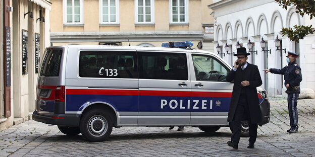 Ein Rabbi läuft in der Nähe einer Synagoge in Wien vor einem Polizisten und einem Einsatzfahrzeug.