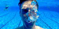 Ein Mann unter Wasser pustet Luft und Blasen tauchen auf.