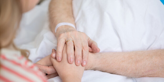 Ein Kind hält die Hände eines Erwachsenen am Krankenhausbett