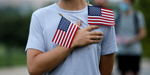 Ein Mann hält zwei USA Flaggen über der lenken Brusthälfte