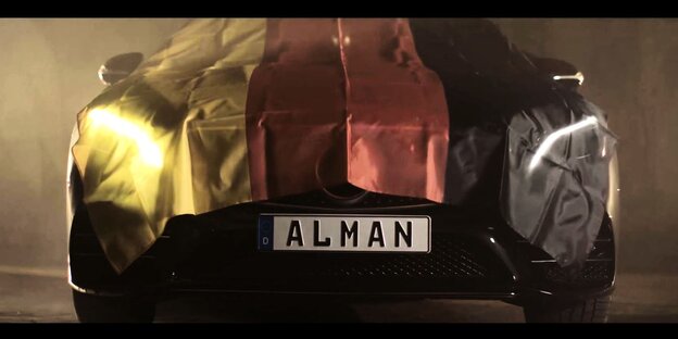 Screenshot aus dem Musikvideo „Alman“ des Rappers Cahmo zeigt einen mit Deutschlandflagge abgedeckten Mercedes bei dem "ALMAN" auf dem Nummernschild steht