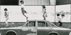 Schwarz-weiß Foto: fünf Kinder springen auf einem Autowrack herum