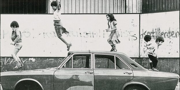 Schwarz-weiß Foto: fünf Kinder springen auf einem Autowrack herum