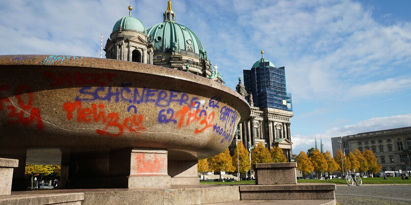 Man sieht die große Granitschale im Lustgarten, die mit neogreller Sprühfarbenschrift bedekckt ist