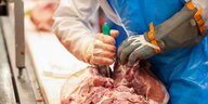 Ein Beschäftigter in der Fleischindustrie zerteilt Fleisch