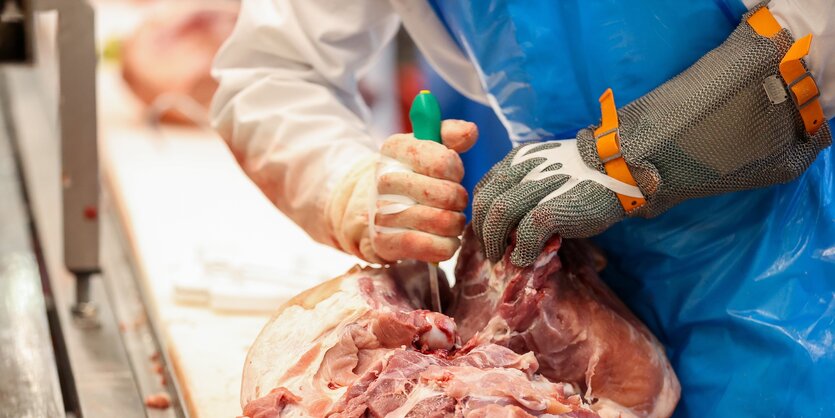 Ein Beschäftigter in der Fleischindustrie zerteilt Fleisch