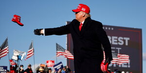 Donald Trump wirft eine rote Mütze bei einer Wahlkampfveranstaltung in die Zuschauermenge
