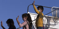 Drei Kinder winken von einer Flugzeugtreppe
