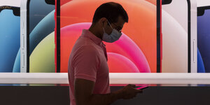 Ein Mann blickt vor einer bunten Smartphone-Werbung auf sein Handy.
