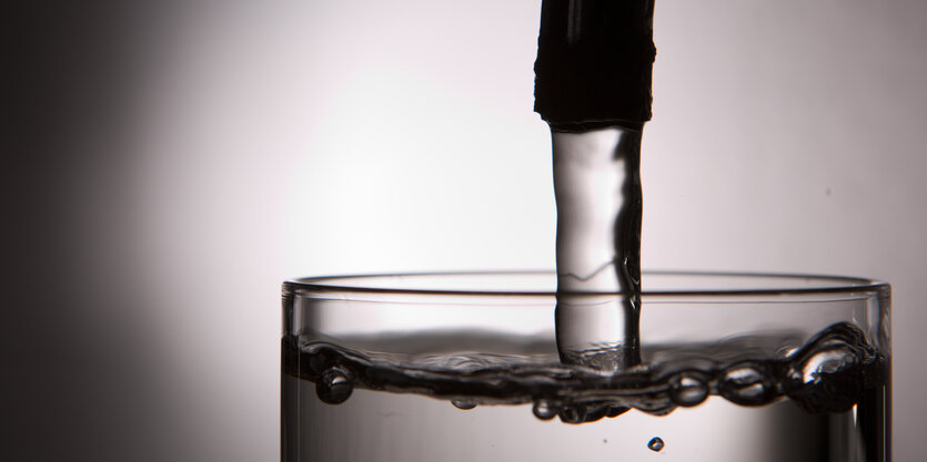 Wasser fließt aus einem Hahn in ein Glas