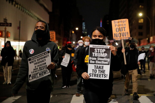 Protesters in face masks walk through the street with anti-Trump signs