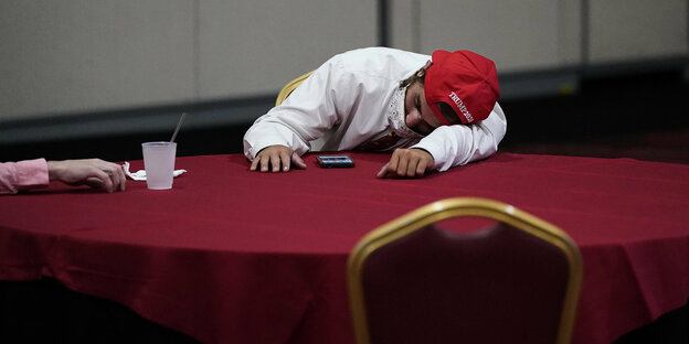 ein Trumpanhänger mit Mütze ist an einem Tisch eingeschlafen